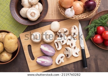 Sliced mushrooms champignon with red onion on wooden cutting board on kitchen. Cooking vegetarian diet dish. Top view, flat lay