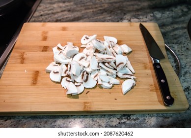 Sliced Mushrooms On A Wooden Cutting Board Next To A Large Knife