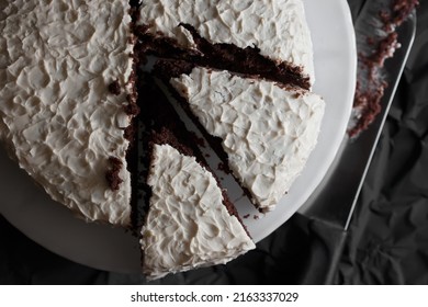 Sliced One Layer Chocolate Cake With White Icing And Knife On Black Background