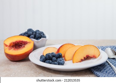 Sliced Peaches And Blueberries Are Served On A White Plate