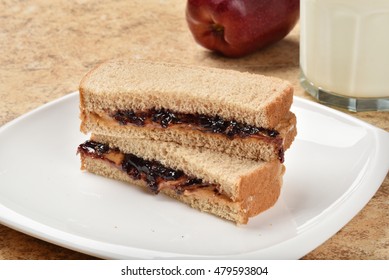 A Sliced Peanut Butter And Jelly Sandwich With An Apple And Milk