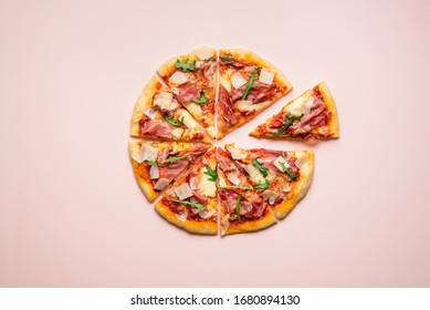 Sliced pizza prosciutto with parmesan and arugula on pink background. Pizza ham and cheese in equal slices top view. Italian traditional food.