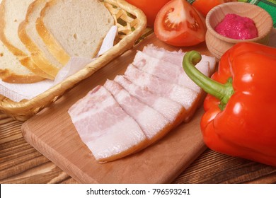 Sliced pork jowl bacon closeup with bread, pepper, tomatoes and horseradish sauce
