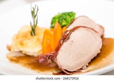 Sliced Pork Tenderloin With Scallopped Potatoes Garnished With Rosemary And Vegetables