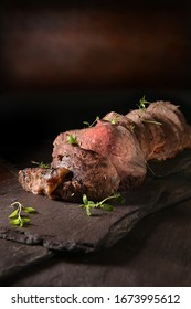 Sliced rare roast beef joint shot against a dark rustic background with thyme herb garnish. Generous accommodation for copy space. - Shutterstock ID 1673995612