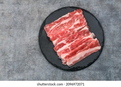 Sliced ​​fresh raw beef. This is beef that most people in the slice call shortplate. Served on black plate on dark background. Close up.
 - Shutterstock ID 2096972071