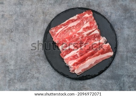 Sliced ​​fresh raw beef. This is beef that most people in the slice call shortplate. Served on black plate on dark background. Close up.

