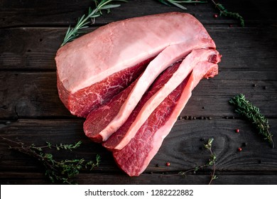 sliced raw piece of marble beef brisket on wooden background, top view