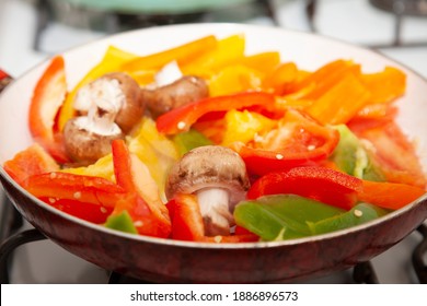 Sliced Red, Yellow, Orange, And Green Bell Peppers And Whole Portabella Mushrooms In A Frying Pan