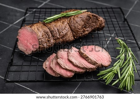 Sliced roast beef cooked medium rare with rosemary and pepper. Juicy roasted beef tenderloin on dark background with copy space