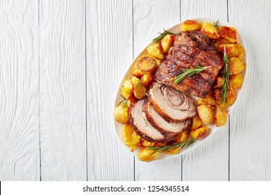 Sliced Roast Pork Roulade -  Porchetta, Delicious Pork Roast With Crusty Roast Potatoes Served On An Oval Dish On White Wooden Table, Close-up, Flatlay, Copy Space