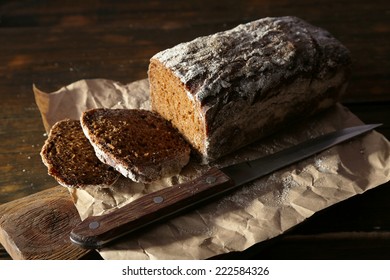 Sliced rye bread and knife on craft paper on cutting board on wooden background