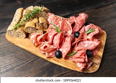 Sliced salumi salami on a wooden board with olives and multigrain baguette.  italian food, appetizer for aperitif or salami sandwich. Top view