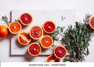 Sliced Sicilian bloody oranges on marble natural background with sprigs of rosemary. Top view. Flat lay.