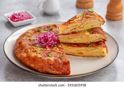 Sliced Spanish potato omelette served on a plate with fresh herbs and pickled red onions.  Selective focus. - Powered by Shutterstock