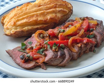 Sliced Steak Covered In A Sauce Of Tomatoes, Peppers, Onions And Seasoning, Accompanied With A Twice Baked Potato