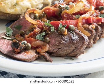 Sliced Steak Covered In A Sauce Of Tomatoes, Peppers, Onions And Seasoning, Accompanied With Twice Baked Potato