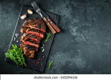 Sliced steak ribeye, grilled with pepper, garlic, salt and thyme served on a slate cutting Board on a dark stone background. Top view with copy space. Flat lay - Shutterstock ID 1432096136