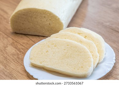 Sliced steamed bread dumpling on white plate with whole dumpling in background on wooden table. Traditional Central European side dish made from yeast dough.
