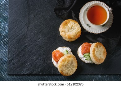 Sliced Traditional English Cheese Scones With Smoked Salmon, Creme Cheese And Fresh Cucumber Served With Whole Scones And Cup Of Tea On Black Slate Texture Background. Top View, Space For Text