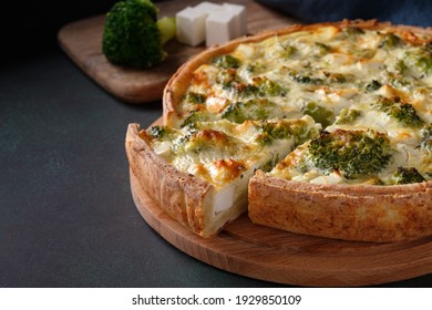Sliced traditional french open quiche pie with feta cheese and broccoli on a dark green background. Copy space, horizontal orientation.