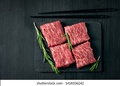 Sliced wagyu marbled beef for yakiniku on plate on black background, Premium Japanese meat and stick, top view and copy space