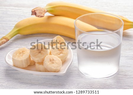 Sliced and whole bananas. On a white plate. On the old wooden table. Misted with clean water. The concept of a healthy lifestyle.