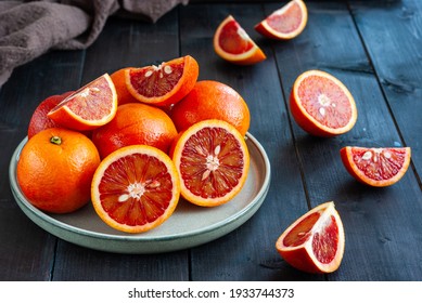 Sliced and whole ripe Sicilian Blood oranges on dark wooden background