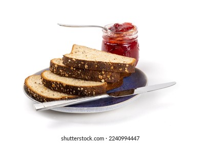 A sliced whole wheat bread on a plate with an open jar of red strawberry or raspberry jam on a spoon isolated on white - Shutterstock ID 2240994447