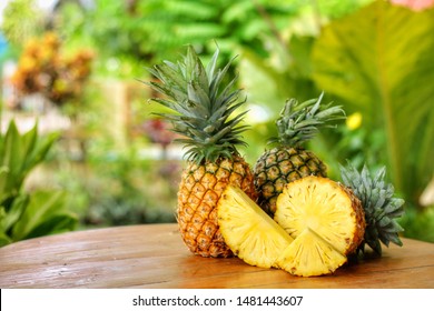 Sliced,half and whole of Pineapple(Ananas comosus) on wooden table with blurred 
 garden background.Sweet,sour and juicy taste.Have a lot of fiber,vitamins C and minerals.Fruits or healthcare concept.