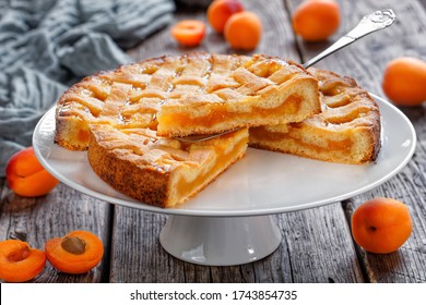 slices of apricot shortcrust pie with a lattice pie crust topping on a cake stand with vintage cake shovel on a rustic wooden table with fresh apricot and grey cloth at the background, landscape view - Shutterstock ID 1743854735