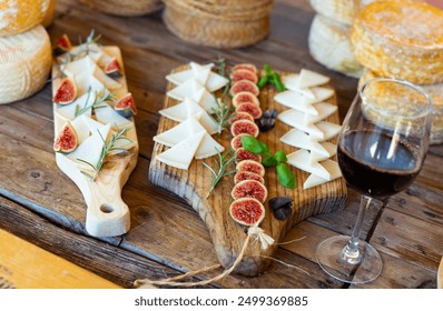 Slices of artisanal goat cheese on wooden boards garnished with fresh ripe figs and fragrant rosemary and basil served with glass of red wine for tasting at Spanish goat farm.. - Powered by Shutterstock