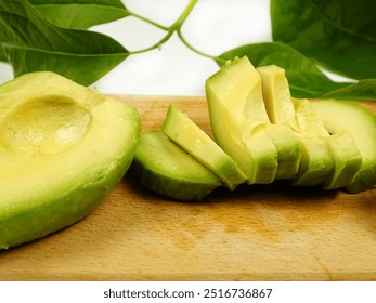 Slices of avocado fruit lie on a wooden cutting board against the background of an avocado leaves - Powered by Shutterstock