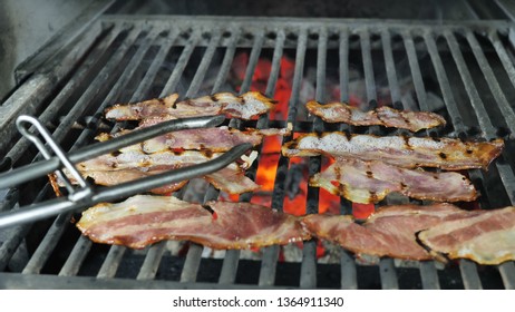 Slices of bacon are grilled, the fat from the bacon is drained from the fried bacon, the chef in black gloves with iron tongs turns over the slices of bacon alternately for the final preparation