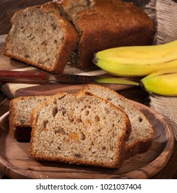 Slices Of Banana Nut Bread On A Wooden Plate With Sliced Loaf And Bananas In Background