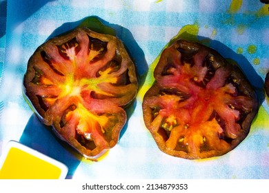 Slices Of Black Heirloom Tomato Drizzled With Blood Orange Fused Olive Oil On Parchment Paper Over Aqua Gingham Cloth From Above