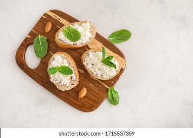 Slices of bread with cottage cheese and mint leaves on wooden cutting board on white background. Top view. Copy space. - Powered by Shutterstock