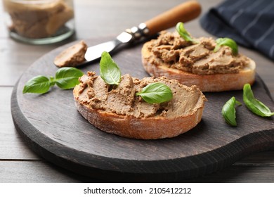 Slices of bread with delicious pate and basil on wooden table, closeup