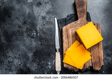 Slices of Cheddar Cheese on a wooden cutting board. black background. Top view. Copy space