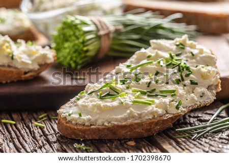 Slices of crusty bread with a cream cheese spread and freshly cut chives on a vintage wooden cutting board.