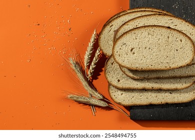 Slices of fresh bread arranged on a dark wooden board with wheat stalks and crumbs scattered against a vibrant orange background. A rustic display perfect for bakery or food-themed concepts - Powered by Shutterstock