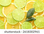 Slices of fresh lemons, limes and green leaves as background, top view
