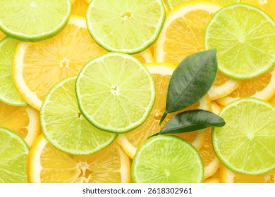 Slices of fresh lemons, limes and green leaves as background, top view