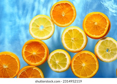 Slices of fresh orange and lemon in water on blue background - Shutterstock ID 2314952119