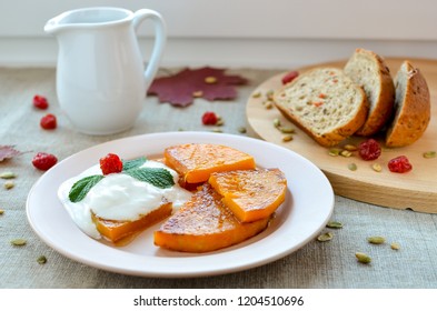 Slices of fried pumpkin with sour cream on a plate. Autumn still life. Pumpkin, bread slices, dried fruit and mint.