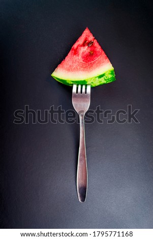 Slices of juicy ripe red watermelon pinned on a fork on a black background