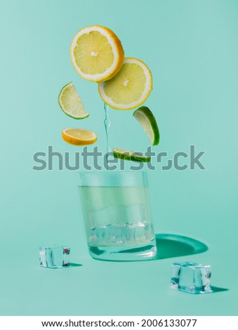 Slices of lemons and lime flying into the glass with ice cubes and water isolated on a pastel mint blue background. Ingredients for a mojito cocktail. Creative refreshing summer drink concept.