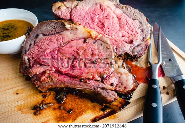 Slices of Medium Rare\
Bone-in Prime Rib with Au Jus: Carved standing prime rib roast on a\
bamboo carving board