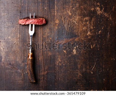 Slices of Medium rare grilled Steak Ribeye on meat fork on dark wooden background