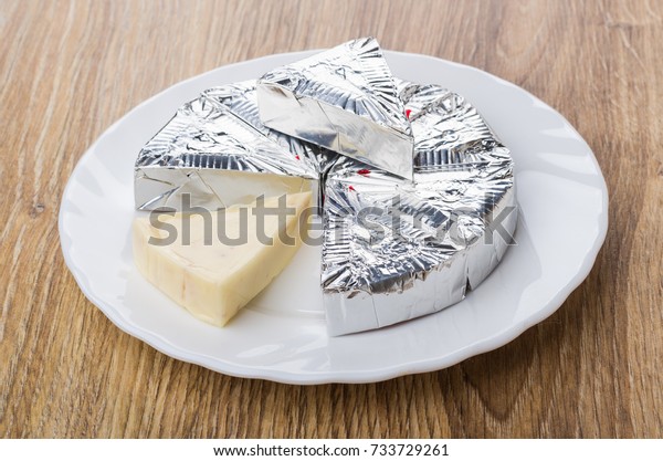 Slices of melted cheese in foil in white plate on\
wooden table